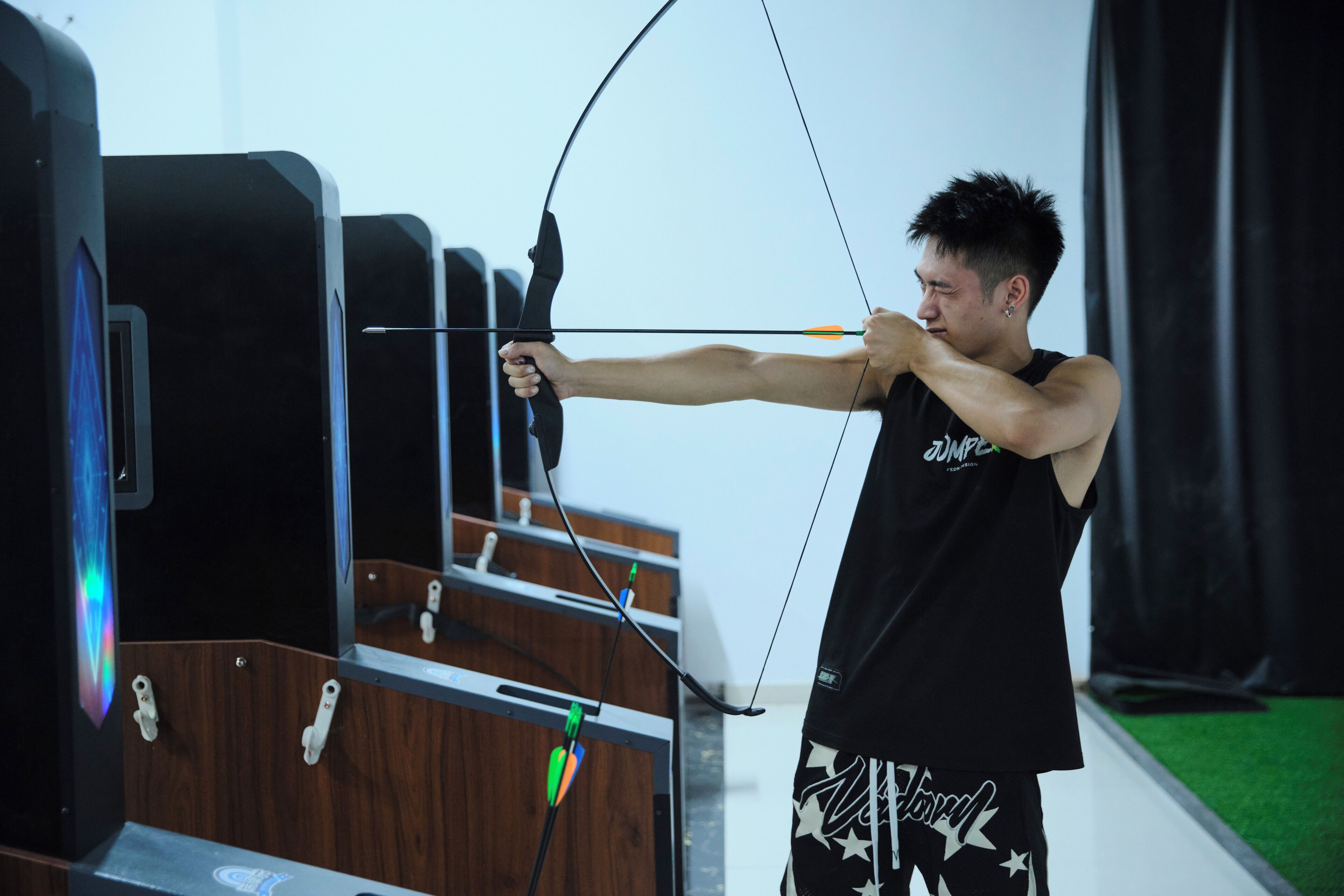 A person aiming a bow at a target in an indoor archery range.