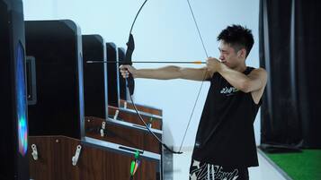 A person aiming a bow at a target in an indoor archery range.