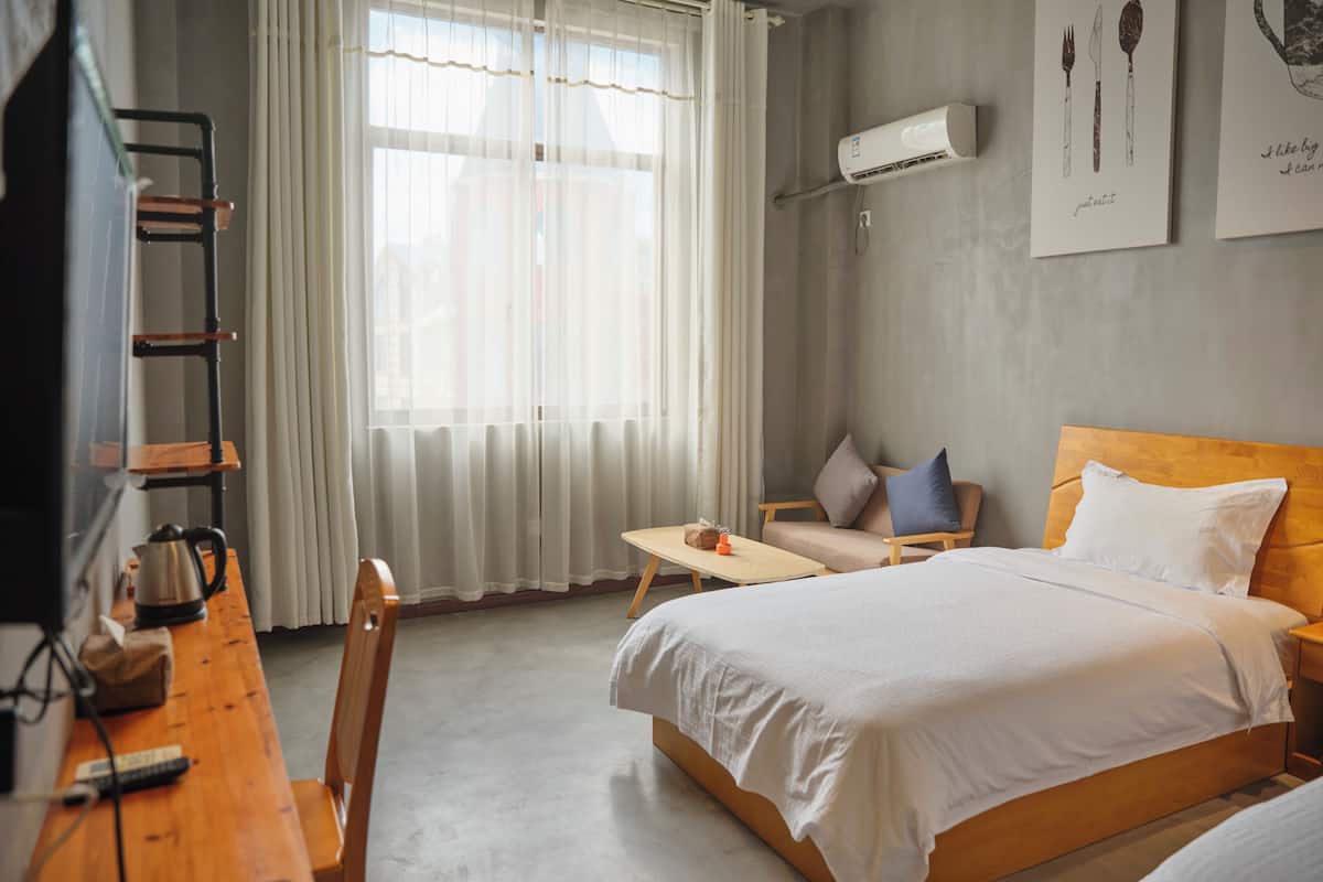 Habitación de hotel con cama, escritorio, silla, mesa y ventana con cortinas.