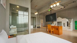 Ein modernes Hotelzimmer mit einem großen Bett, einem Schreibtisch mit Stuhl, einem Fernseher und einer kleinen Spielecke.