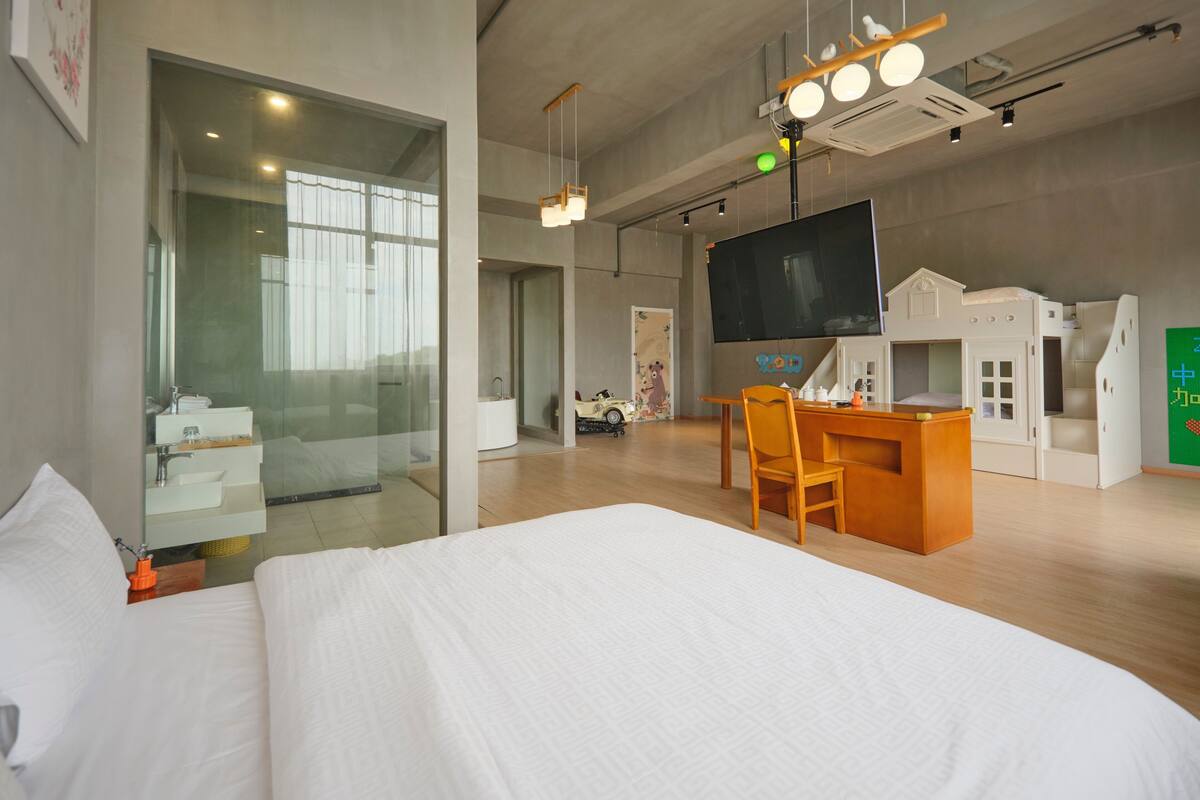 Una habitación de hotel moderna con una cama grande, un escritorio con silla, un televisor y una pequeña zona de juegos.