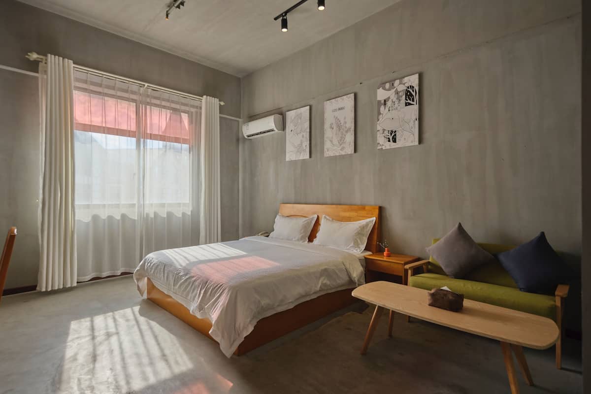 Un dormitorio moderno con una cama grande, un sofá verde, un banco de madera y obras de arte en las paredes.
