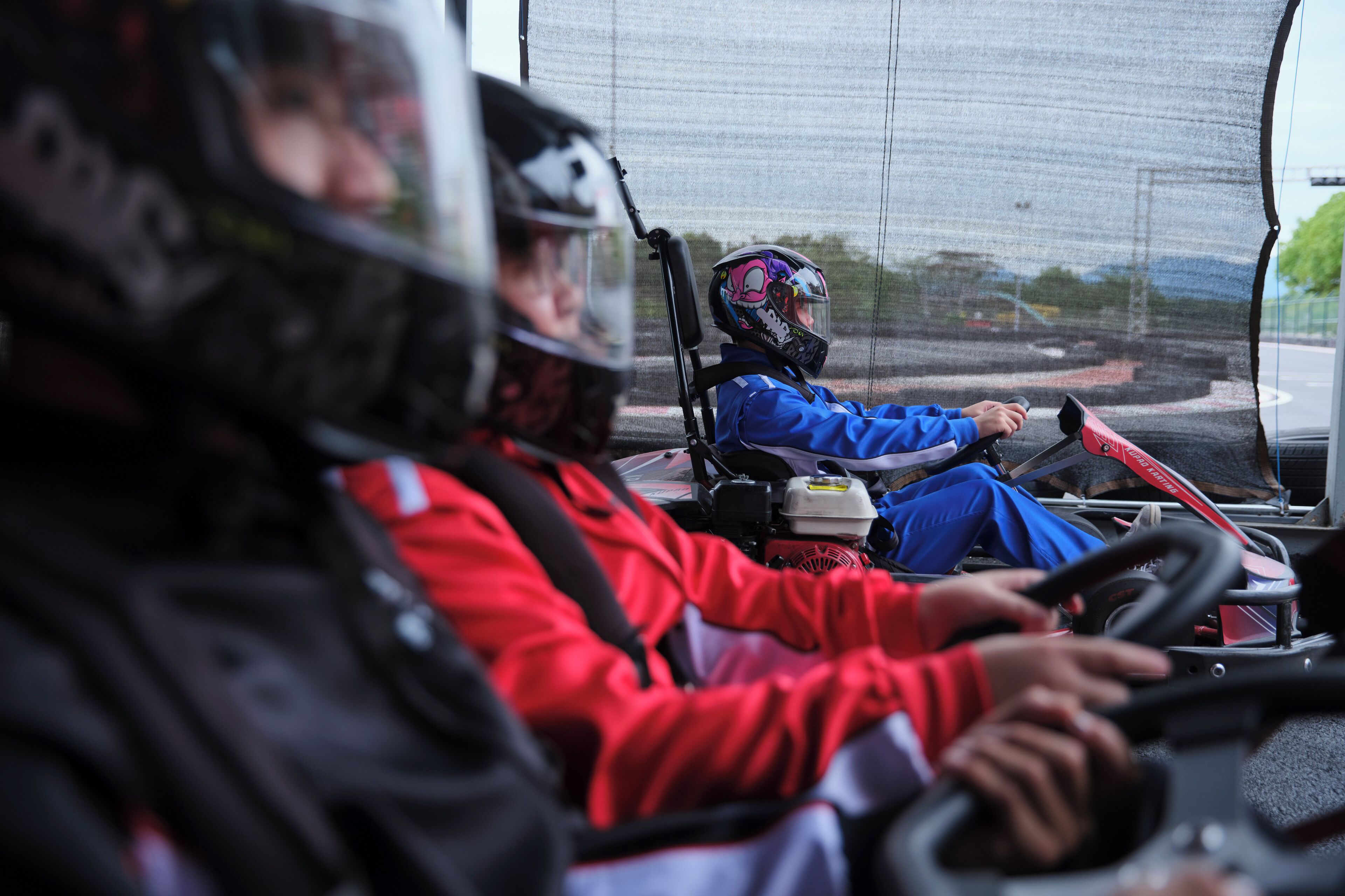 Interior de veículo com duas pessoas, uma usando jaqueta vermelha e outra jaqueta azul, ambas com capacete.
