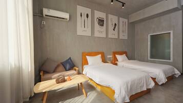 A modern hotel room with two beds, a small sofa, a wooden table, and artwork on the wall.
