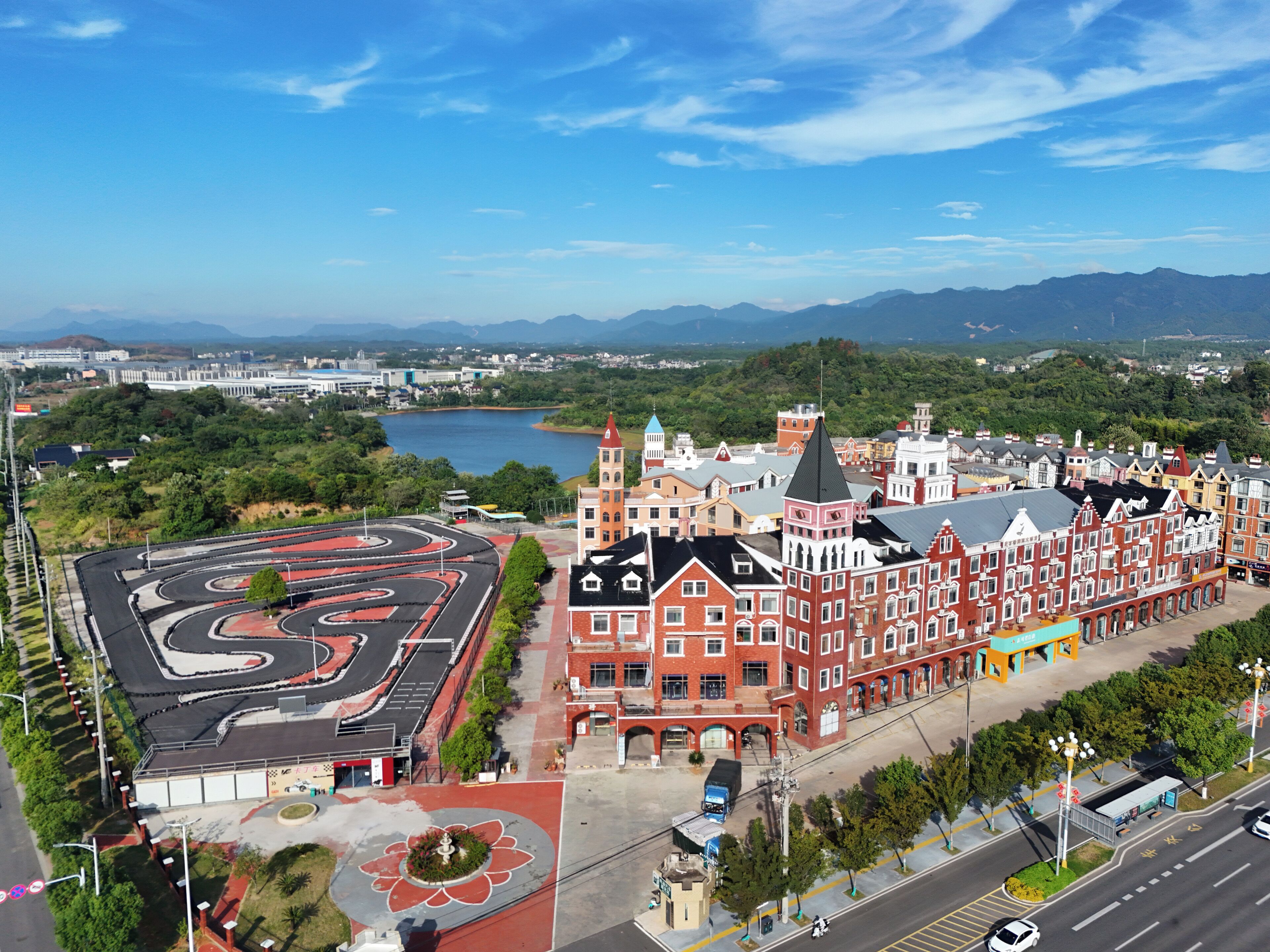A large, historic building with red brick facades and multiple stories, surrounded by lush greenery and a winding road.