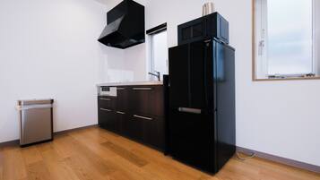 A modern kitchen with a stainless steel dishwasher, dark wooden cabinets, a black refrigerator, and a black range hood.