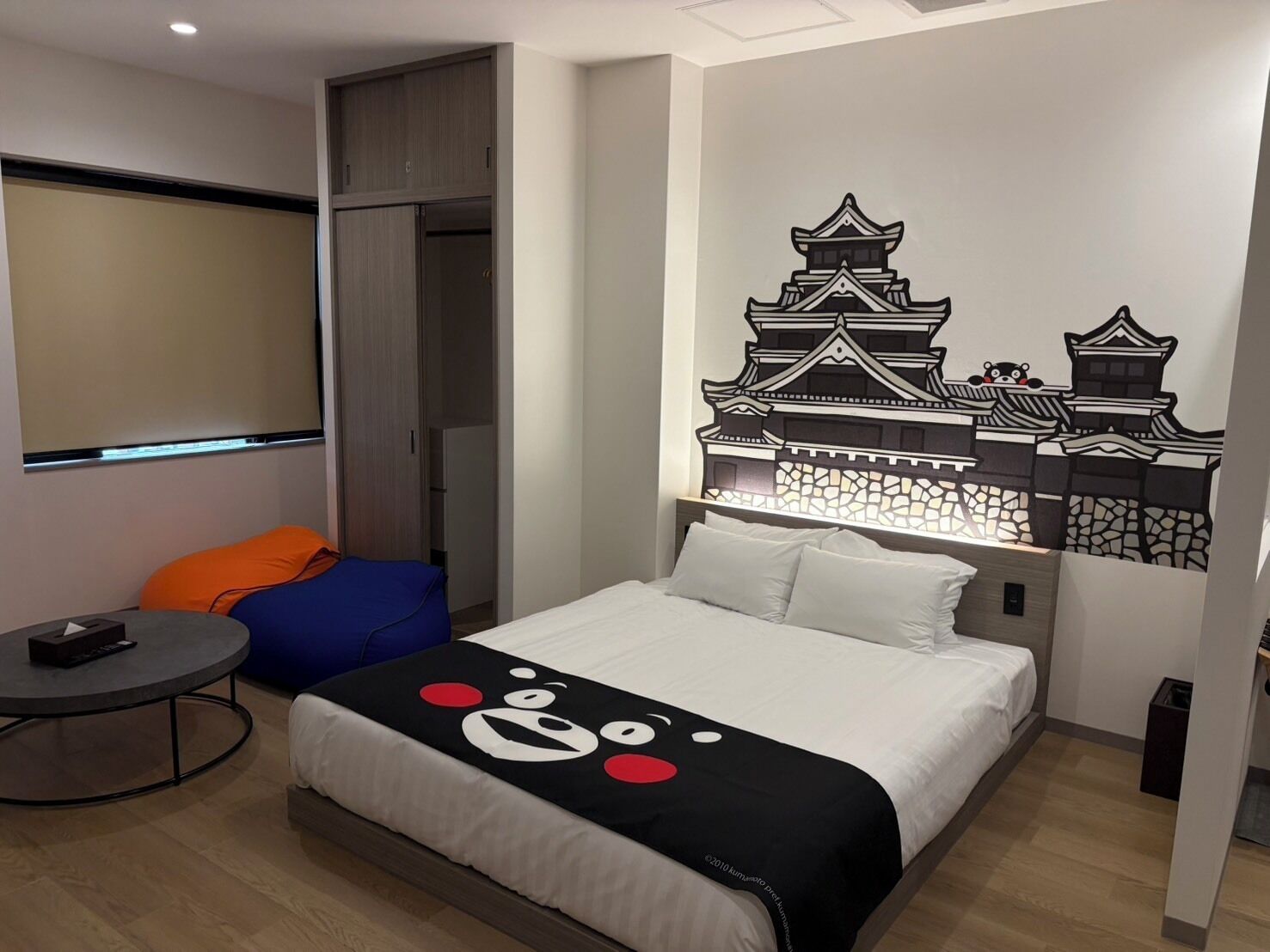 A hotel room with a bed, a round table, a sofa, and a wall with a Japanese castle mural.
