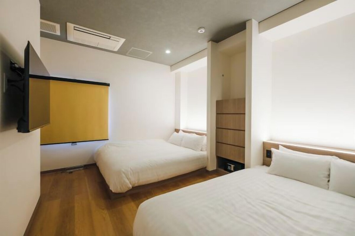 A hotel room with two beds, a TV mounted on the wall, and a wooden cabinet.