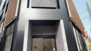 Entrada de un hotel moderno con puerta de vidrio y un interior visible que incluye una escalera y un extintor.