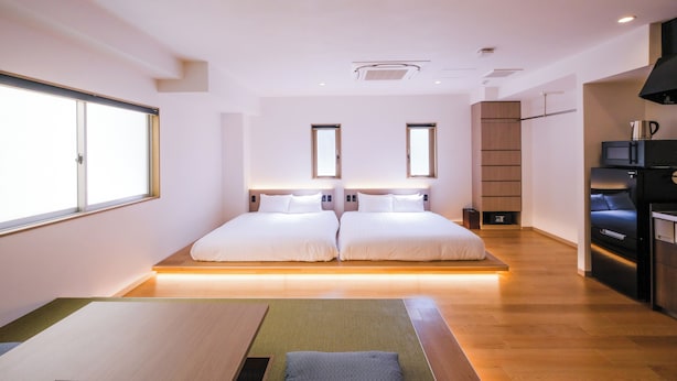 Una habitación de hotel moderna con dos camas, kitchenette y un ventanal grande.