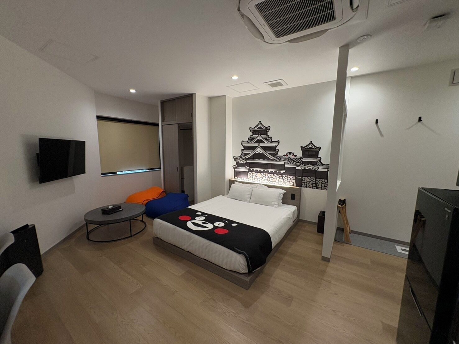 A modern hotel room with a bed, a TV, a small table, and a wall-mounted air conditioner.