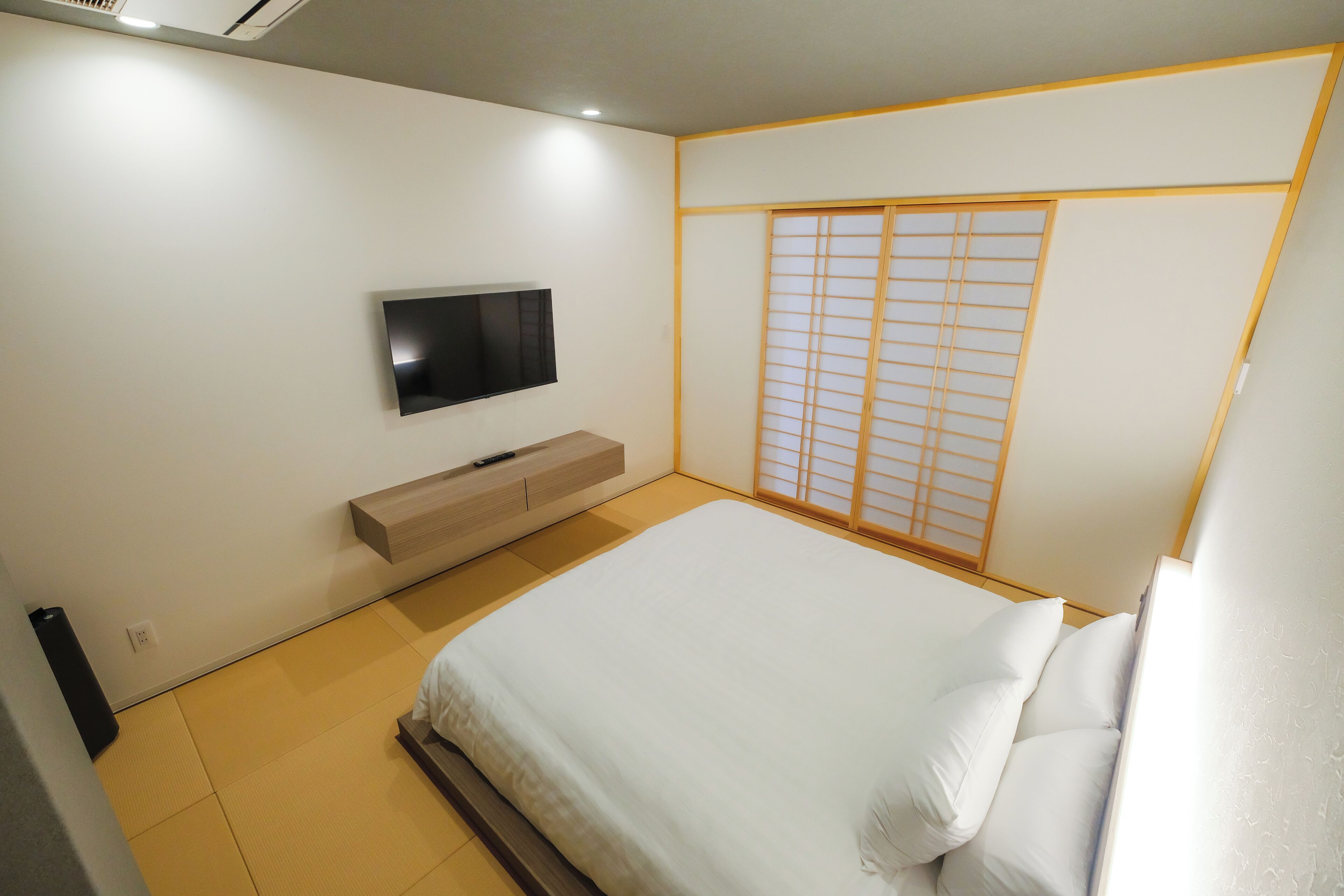 Un dormitorio con una cama, un televisor montado en la pared, un armario corredero y un pequeño mueble de madera.