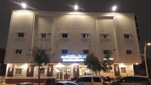 Un hotel de varios pisos con una entrada central, señalización iluminada y un estacionamiento al frente.