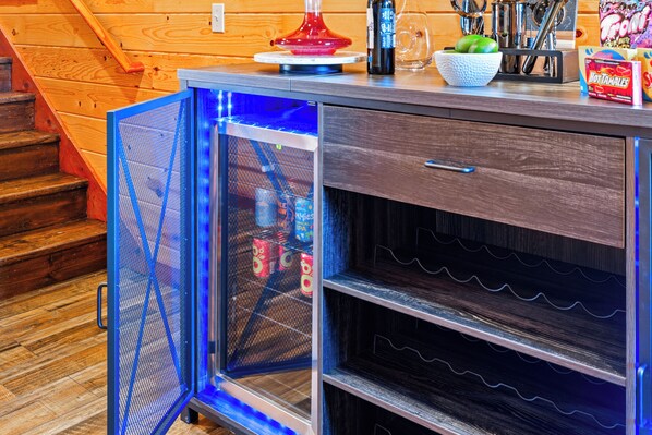 Una cocina con escalera de madera, refrigerador con puerta de vidrio y encimera con diversos objetos.