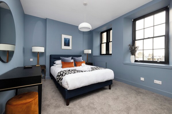 A bedroom with a bed, bedside tables, a desk, a window with a view, and a hanging light fixture. - Stylish 2-bed flat in New Town (Edinburgh)