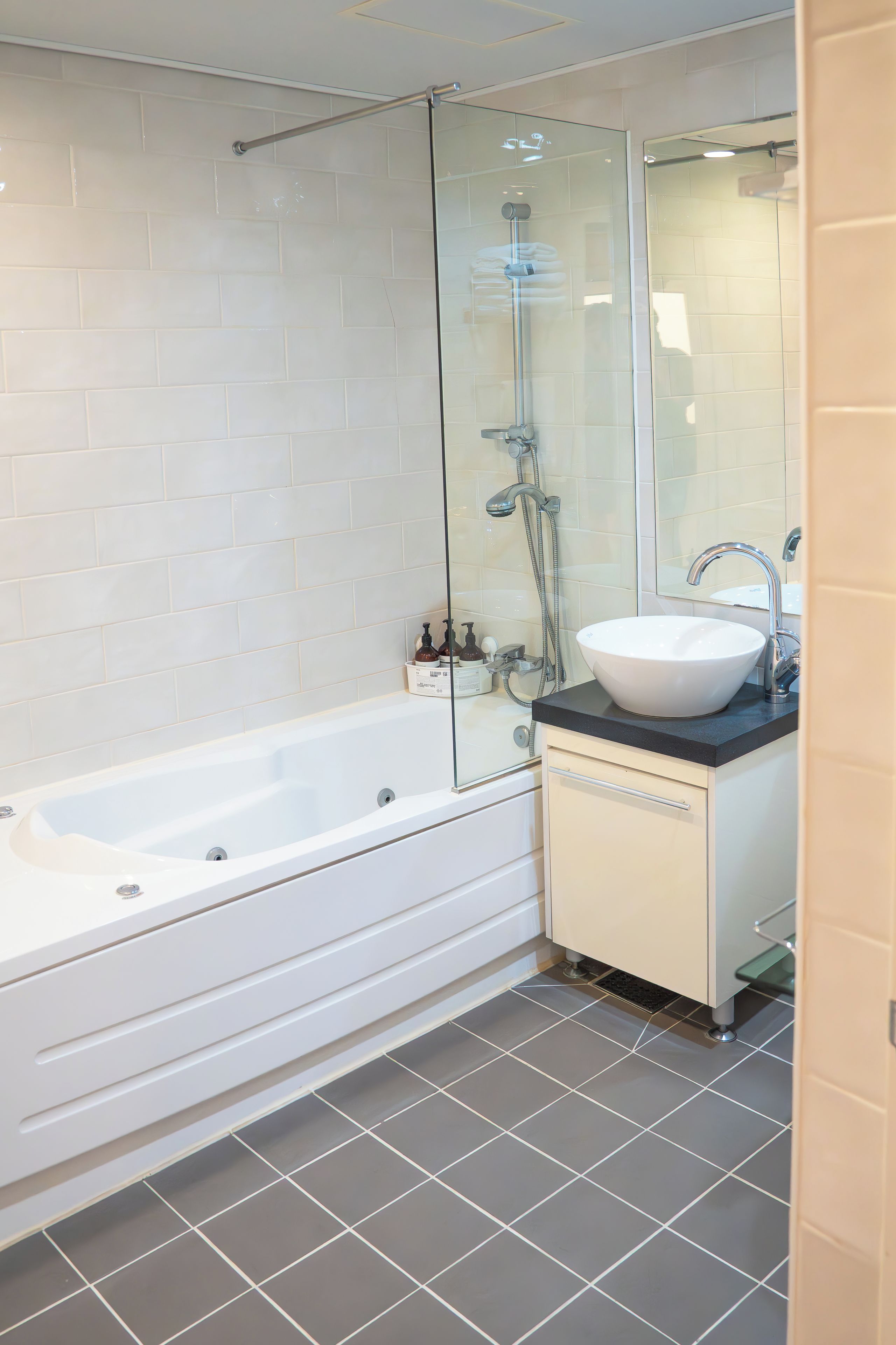 A modern bathroom with a glass-enclosed shower, a white bathtub, and a sink with a black countertop.