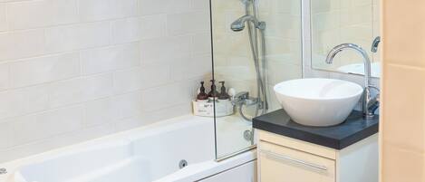 A modern bathroom with a glass-enclosed shower, a white bathtub, and a sink with a black countertop.