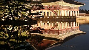 A traditional building with a reflection in the water, surrounded by trees.