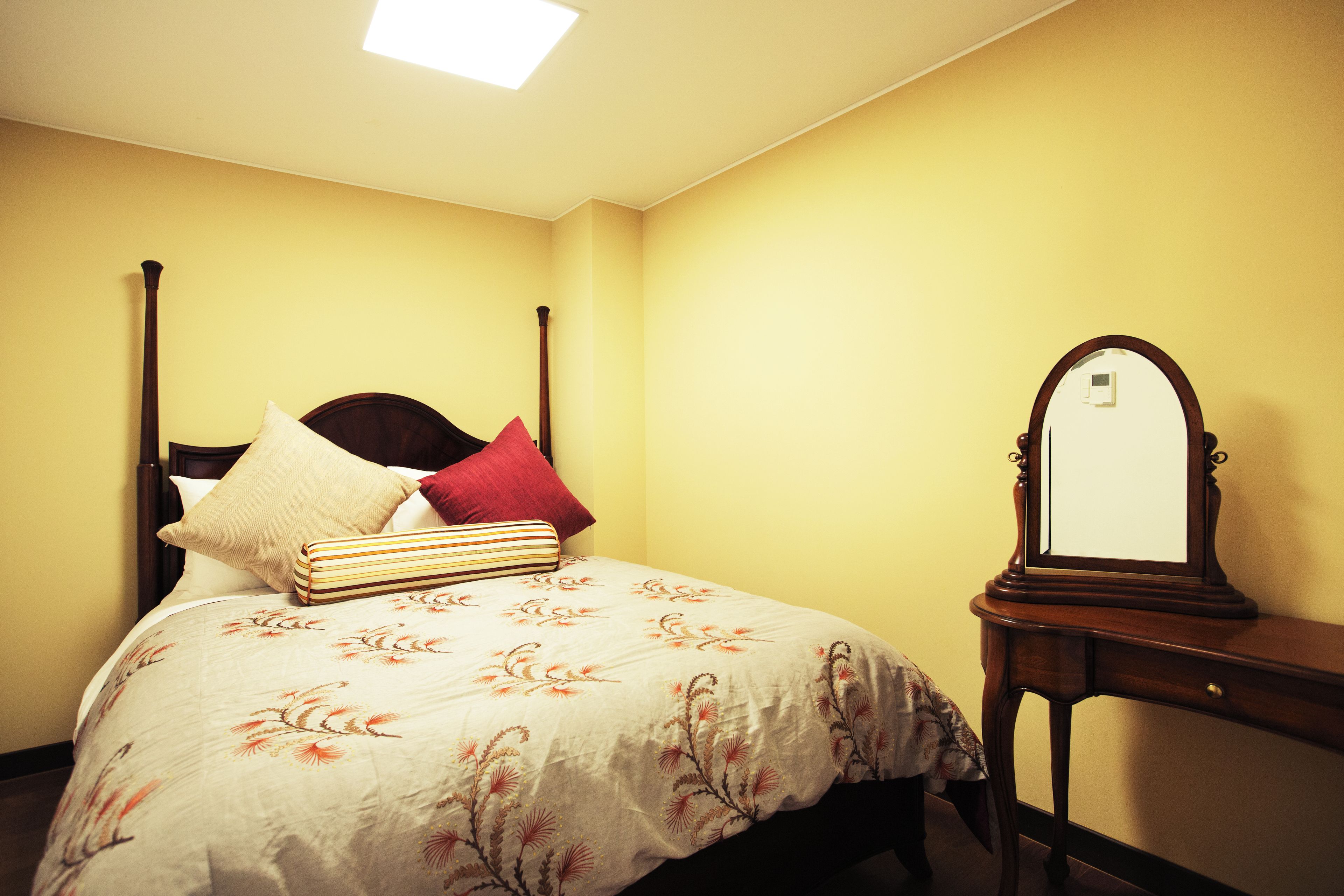 A bedroom with a four-poster bed, a bedside table with a mirror, and a floral bedspread.