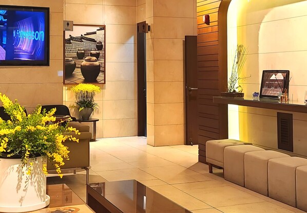 Una moderna zona de recepción con televisor de pantalla plana, mostrador de recepción, área de descanso y una planta en maceta.