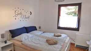 Une chambre avec deux lits, une table de chevet avec une lampe, une fenêtre donnant sur un beau paysage et un élément décoratif mural.