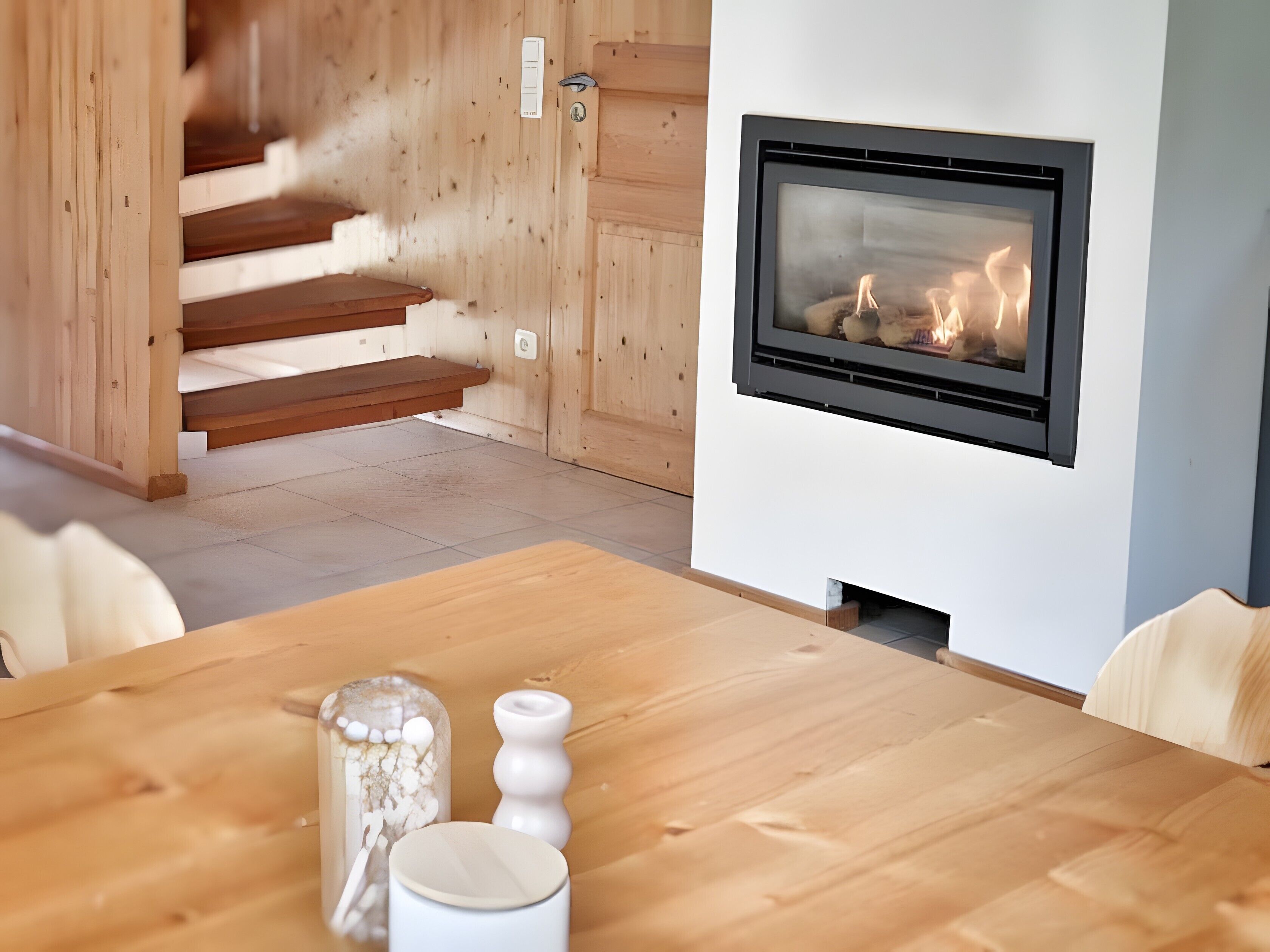 Un interior moderno con chimenea, escalera de madera y una mesa de comedor con objetos decorativos.