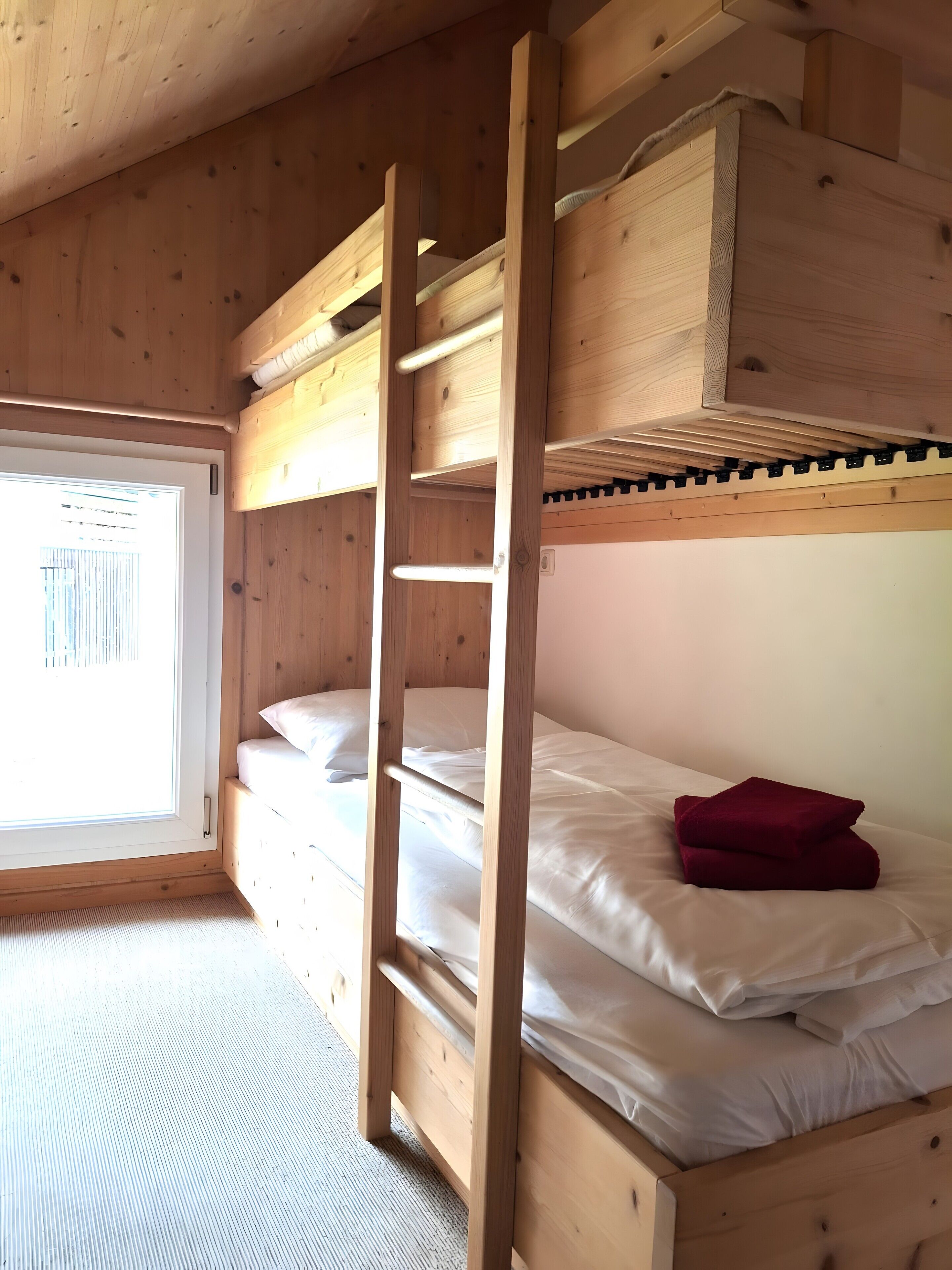 A bunk bed room with a window, wooden walls, and a carpeted floor.