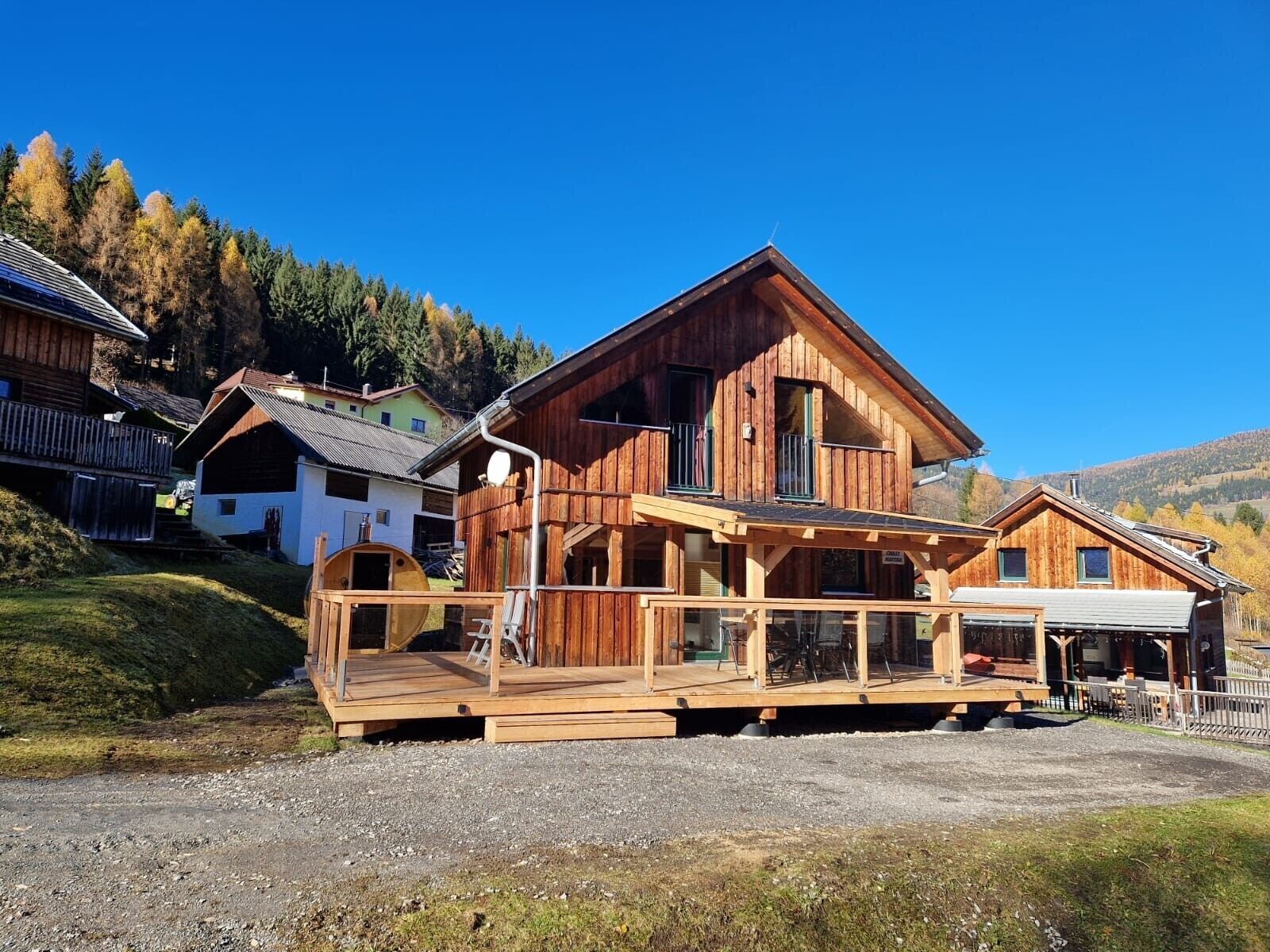 A wooden chalet with a deck, surrounded by a forest and hills.