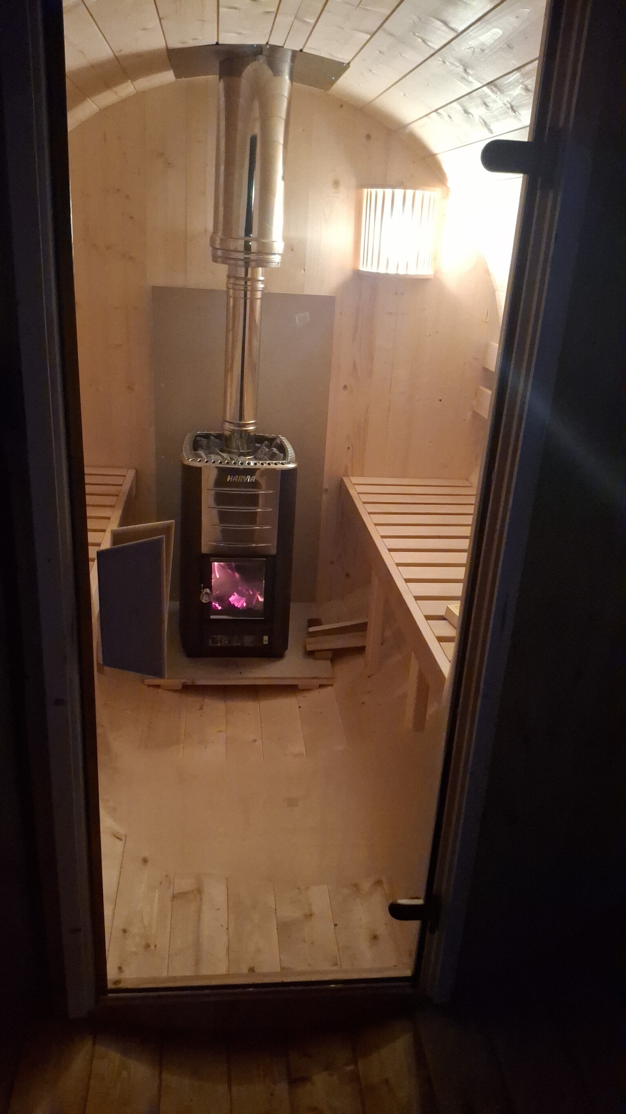 A sauna room with a Harma sauna heater, wooden benches, and a sloped ceiling.