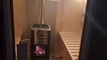 A sauna room with a Harma sauna heater, wooden benches, and a sloped ceiling.