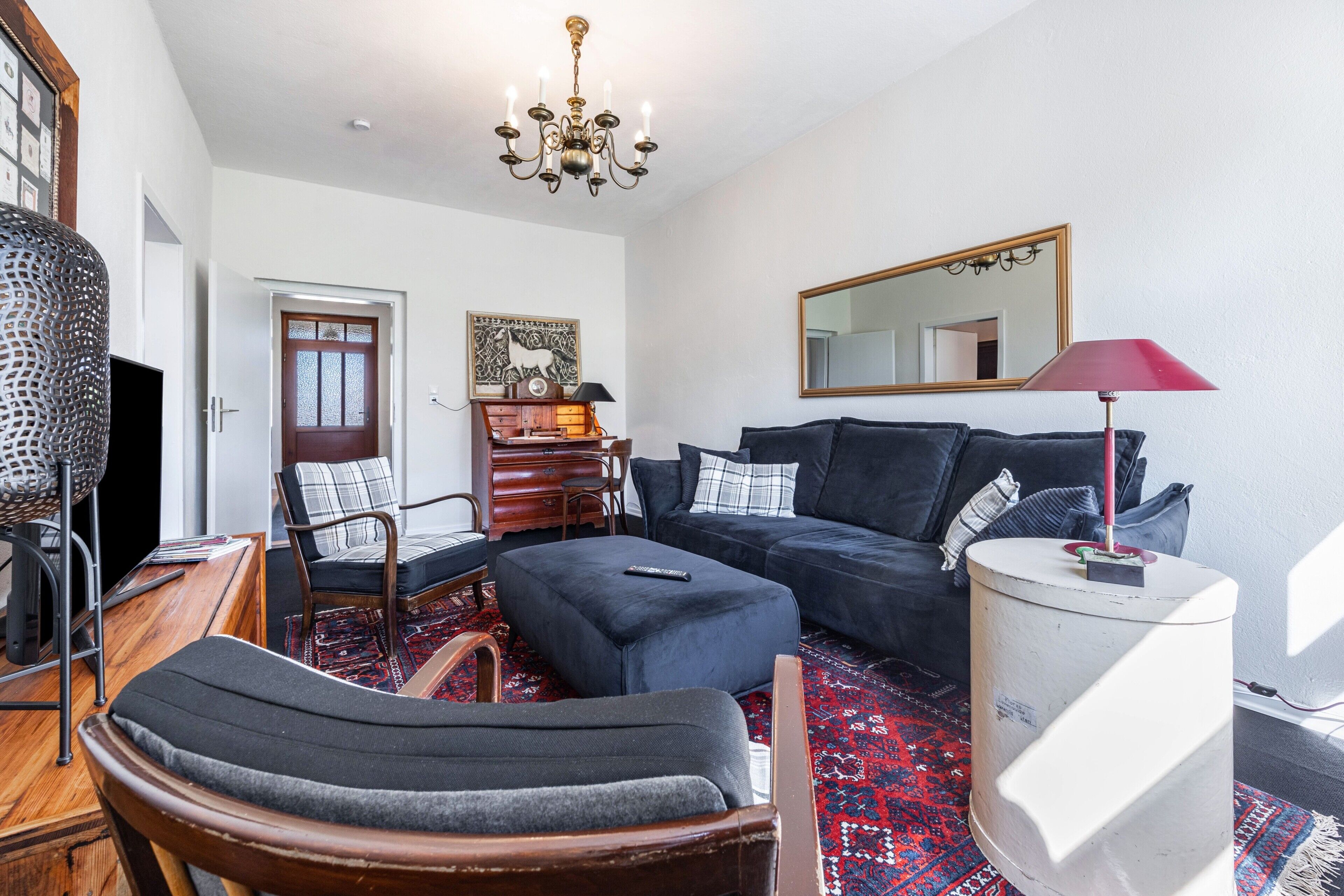 A living room with a sofa, ottoman, and a chair. There is a wooden cabinet, a television, and a chandelier.