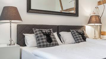 Een netjes opgemaakt bed met twee kussens, een bedlampje en een spiegel aan de muur.