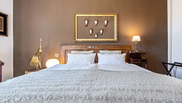 A neatly made bed with white linens, a headboard with a wooden finish, a framed picture of animal skulls on the wall, and a lamp on a bedside table. - Holiday Apartment 'Landhaus Heiddorf' with 2 Comfortable Bedrooms, Terrace with BBQ & Sun Loungers (Neu Kaliß)
