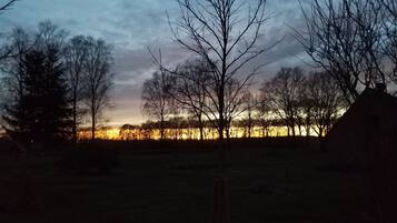 A landscape with trees and a distant view of a body of water during twilight.