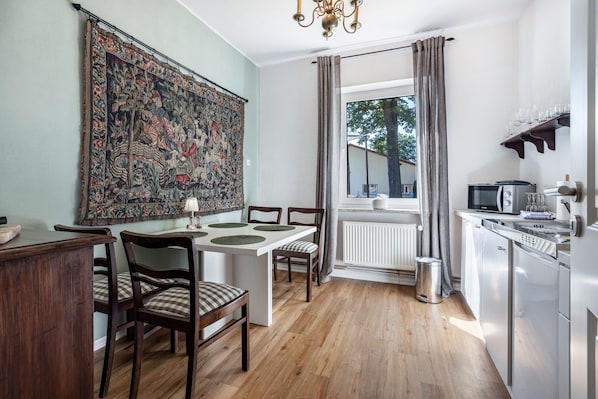A dining area with a table, chairs, a chandelier, a tapestry, and a view through a window. - Holiday Apartment 'Landhaus Heiddorf' with 2 Comfortable Bedrooms, Terrace with BBQ & Sun Loungers (Neu Kaliß)