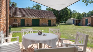 A patio with a round table and four chairs, a brick building with green doors in the background, and a grassy area. - Holiday Apartment 'Landhaus Heiddorf' with 2 Comfortable Bedrooms, Terrace with BBQ & Sun Loungers (Neu Kaliß)