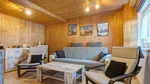 A wooden-paneled room with a sofa, armchair, coffee table, and a small table with decorative items.