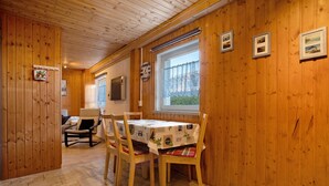 A wooden-paneled room with a dining table, chairs, a sofa, and a window with a view.