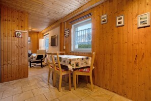A wooden-paneled room with a dining table, chairs, a sofa, and a window with a view.