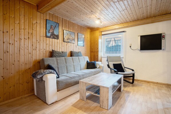 Una habitación acogedora con paredes de madera, un sofá, una mesa de centro, una silla y un televisor.