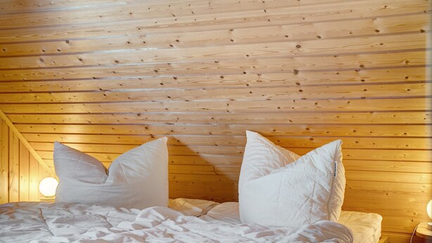 A wooden-paneled room with a bed, pillows, and a nightstand with a lamp.