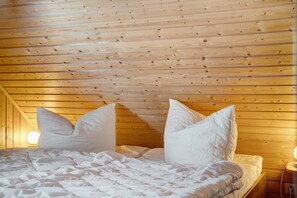 Een kamer met houten lambrisering, een bed, kussens en een nachtkastje met een lamp.