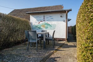 Un patio con una mesa y sillas, un mural en la pared y un seto.