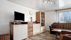 A modern living room with a flat-screen TV, wooden cabinets, a sofa, and a dining table. - Apartment 'Am Darß - Kogge' with Private Terrace, Private Garden and Wi-Fi (Pruchten)