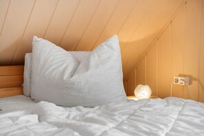 Une chambre à coucher avec une tête de lit en bois, du linge de lit blanc et une table de chevet avec une lampe.