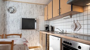 A kitchen with wooden cabinets, a dishwasher, an oven, a coffee maker, and a clock on the wall. - Apartment 'Am Darß - Kogge' with Private Terrace, Private Garden and Wi-Fi (Pruchten)