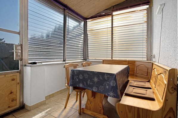 A compact room with a table, chairs, a bench, and large windows with blinds.