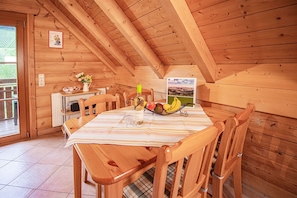 Un comedor de madera con una mesa dispuesta para dos personas, una botella y una cesta de frutas.