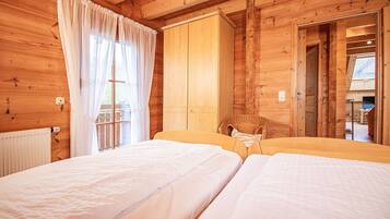Ein Zimmer in einer Holzhütte mit zwei Betten, einem Korbstuhl und einem großen Fenster mit Vorhängen.