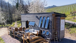 A modern, compact wooden building with a patio area, outdoor seating, and a small garden.